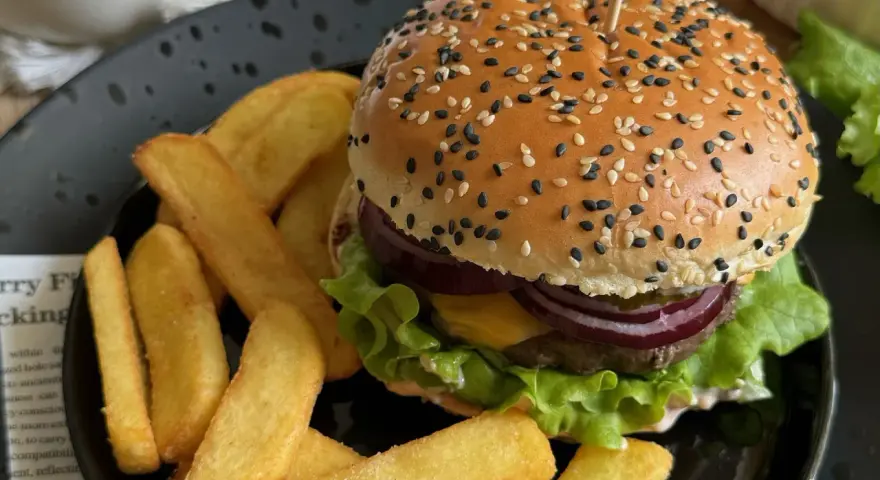 Soczysty burger z sezamem i frytki na czarnym talerzu.