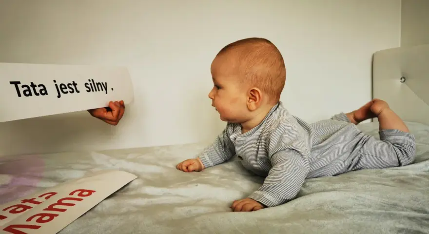 10 tygodniowe dziecko leży na brzuchu, patrząc na napis "Tata jest silny".