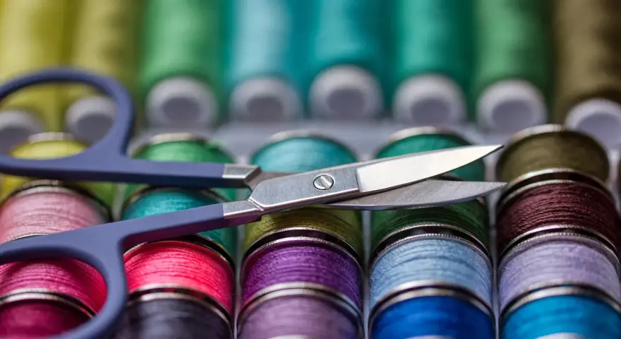 Ciseaux sur une rangée de bobines de fil à coudre aux couleurs vives. Le grosseur de fil à coudre varie, offrant un arc-en-ciel de possibilités créatives.