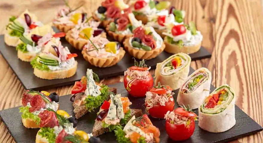 Varietà di tartine, involtini e pomodorini ripieni, perfette per idee aperitivo economico e gustoso.