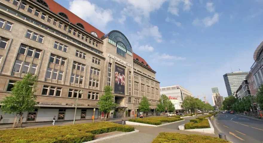 Das KaDeWe Berlin, ein imposantes Gebäude mit vielen Fenstern, steht unter einem blauen Himmel mit Wolken.