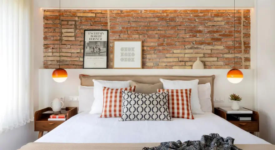 Ideas para decorar la pared de la cabecera de la cama: ladrillo visto, cuadros y lámparas naranjas.