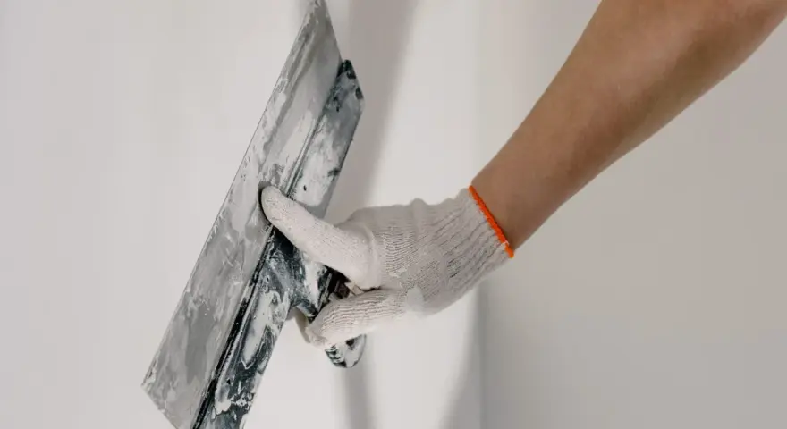 Mano enguantada alisando masilla para tapar agujeros en la pared.