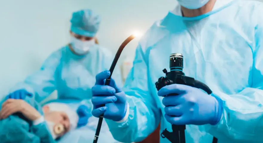 Lekarz w niebieskich rękawiczkach trzyma endoskop podczas gastroskopii.