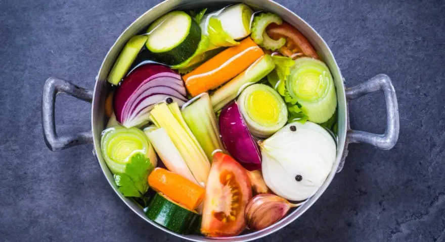 Olla con verduras cortadas en trozos: cebolla, zanahoria, calabacín, puerro, tomate y ajo.