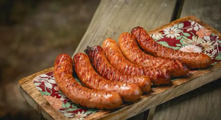 Apetyczna kiełbasa z grilla, rumiana i soczysta, ułożona na drewnianej desce z kolorowym wzorem.