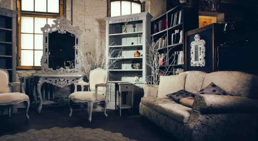 Salotto con divano, poltrone, specchio barocco e librerie. Un esempio di arredamento massimalista che unisce elementi classici e decorazioni elaborate.