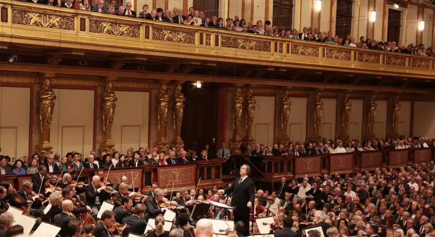 Un director dirige una orquesta sinfónica ante un público entusiasta, interpretando obras de Beethoven en un teatro majestuoso.