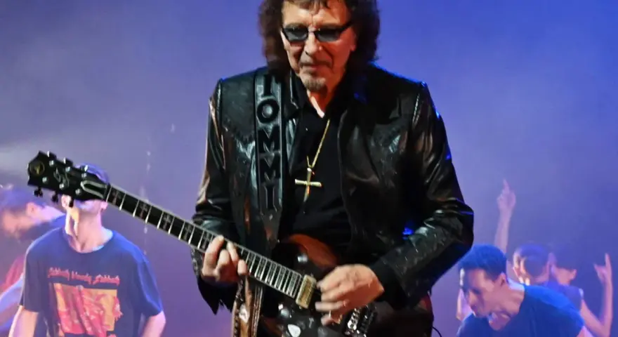 Tony Iommi, Gitarrist von Black Sabbath, spielt auf der Bühne. Im Hintergrund jubelt das Publikum.