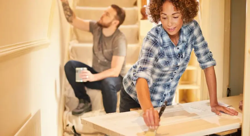 Pareja renovando su hogar con una reforma sin obras. Ella pinta una puerta, él la pared.