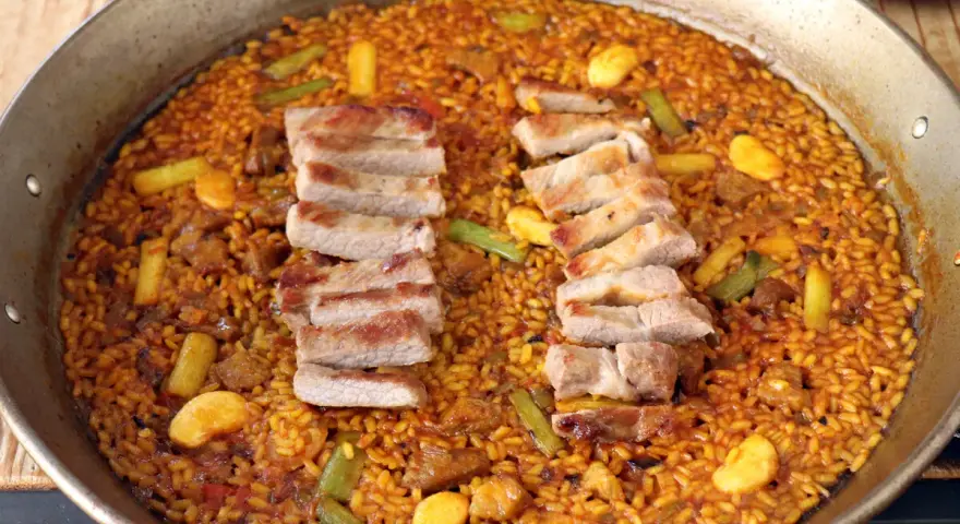 Arroz con secreto, un plato de paella con cerdo tierno y verduras crujientes, listo para ser disfrutado.