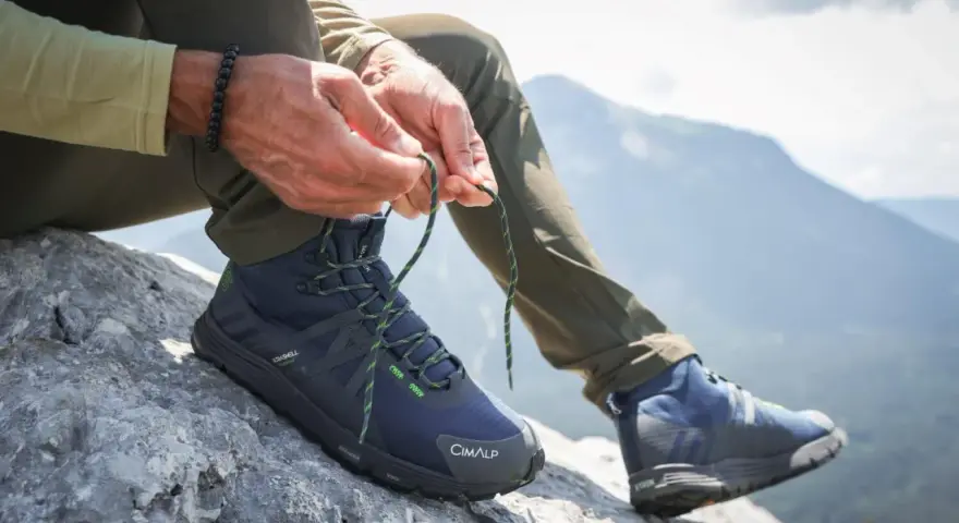 Uomo lega i lacci di scarponi da hiking su roccia, pronto per il trekking in montagna.