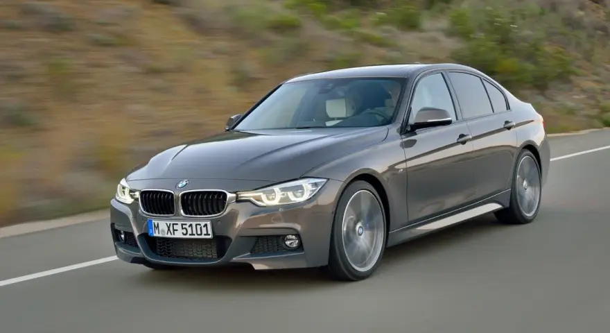 Szary sedan BMW F30 z dynamicznymi silnikami pędzi po drodze, ukazując sportowy charakter.