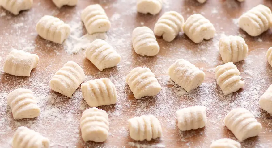 Gnocchi di ricotta freschi, pronti per essere cucinati, spolverati di farina su un tagliere di legno.