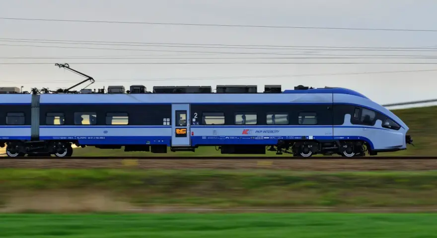 Pociąg PKP Intercity w ruchu, z widocznymi oknami i logo przewoźnika.