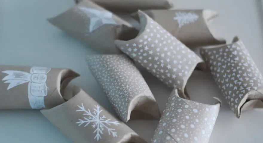 En adventskalender av toarullar, dekorerade med vita julmotiv som snöflingor och stjärnor. Perfekt för att skapa egna små överraskningar.