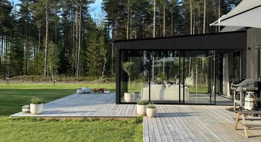 Modernt uterum med glaspartier och träaltan, perfekt för att bygga ett drömhem vid skogen.