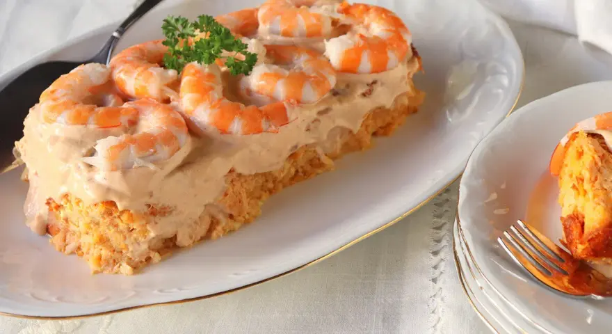 Delicioso pudin de pescado cubierto con crema y camarones, decorado con perejil.