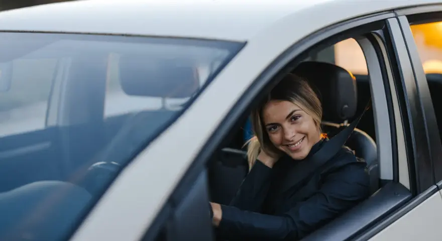 Uśmiechnięta kobieta w samochodzie, zapięta pasami. Czas oczekiwania na prawo jazdy minął, teraz czas na jazdę!