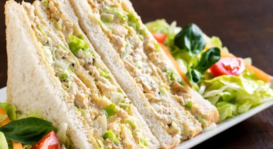 Sándwich de pollo cortado en triángulos, relleno de pollo desmenuzado y lechuga, acompañado de ensalada fresca.