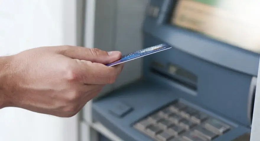 Dłoń z kartą zbliża się do bankomatu. Może to być związane z obsługą konta w Credit Agricole, a nie z zajęciami komorniczymi.