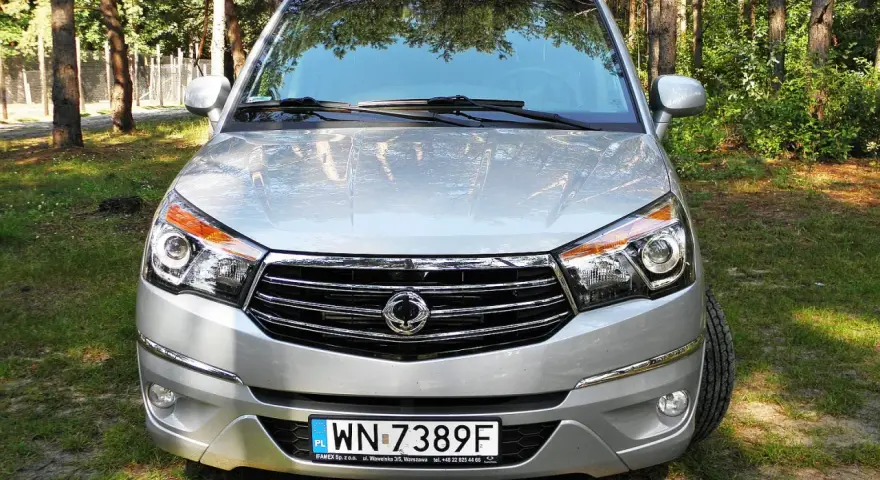 Srebrny SsangYong Rodius z przodu, zaparkowany na tle lasu.