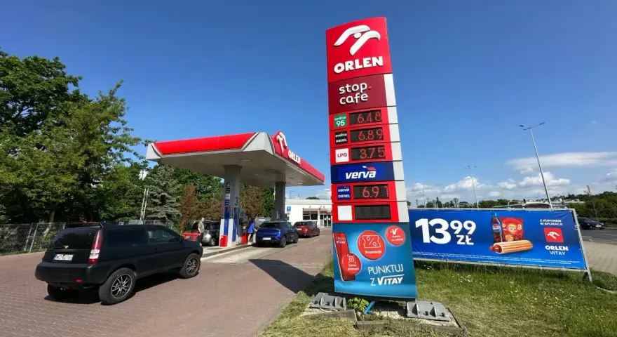 Stacja paliw Orlen z cennikiem paliw: benzyna 95 za 6.48 zł, diesel za 6.89 zł, LPG za 3.75 zł. Obok reklama hot doga i napoju.