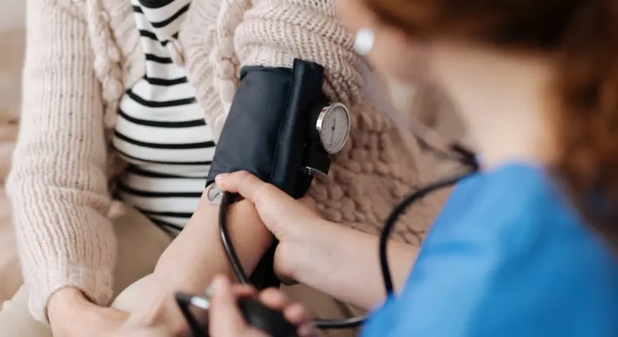 Pielęgniarka mierzy ciśnienie kobiecie w ciąży. Monitorowanie podwyższonego ciśnienia pod koniec ciąży jest kluczowe dla zdrowia mamy i dziecka.
