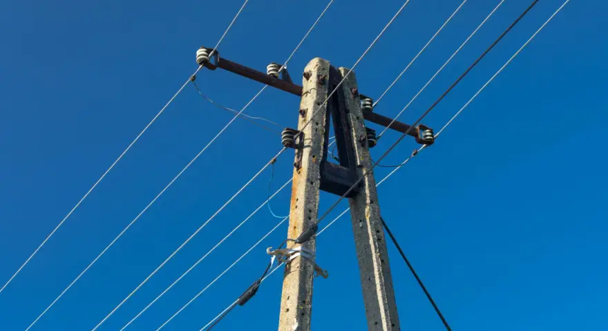 Słup energetyczny z przewodami na tle błękitnego nieba. Zastanawiasz się, ile wynosi odszkodowanie za słupy energetyczne na działce?