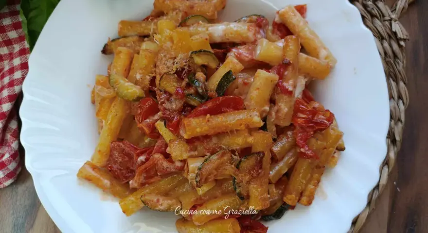 Piatto di pasta con zucchine e pomodorini, condita con formaggio grattugiato e basilico fresco.