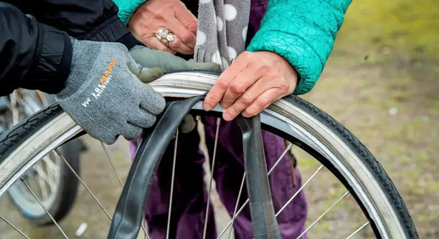 Två personer byter cykelslang. En med grå handske och en med grön jacka och prickig scarf.