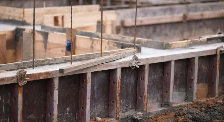 Drewniany szalunek czeka na beton. Widać zbrojenie i świeży beton.