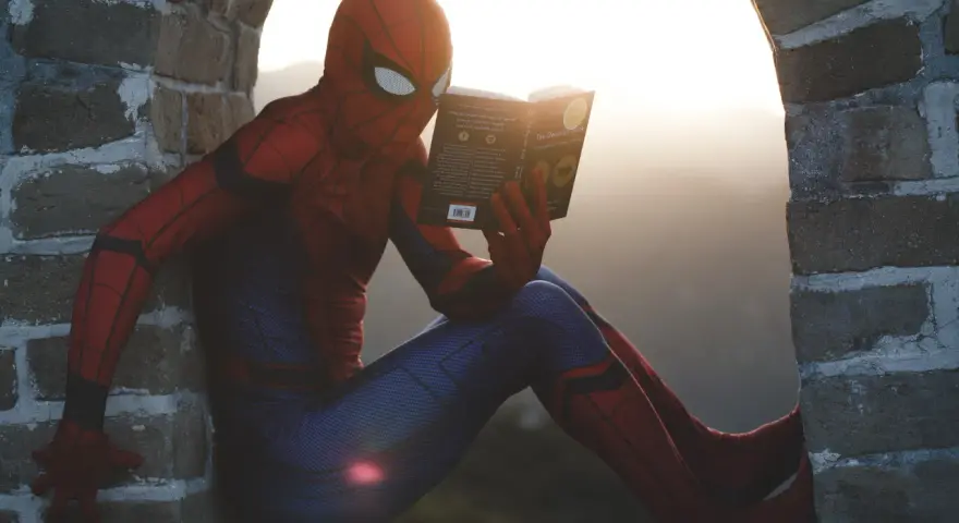 Spider-Man w czerwonym stroju siedzi na murze i czyta książkę. Czy komiks to utwór literacki? Nawet superbohaterowie potrzebują chwili wytchnienia i wiedzy.