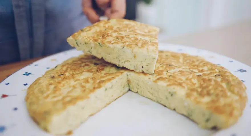 Una fetta di frittata, preparata con la ricetta perfetta, viene sollevata da un piatto decorato.