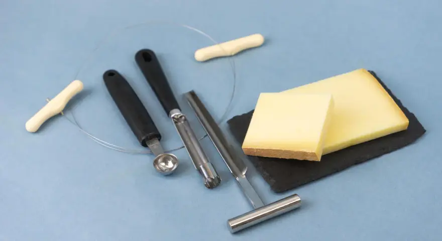 Des morceaux de fromage, des outils pour le découper et une ficelle. L'origine du fromage la dent du chat est un mystère savoureux.