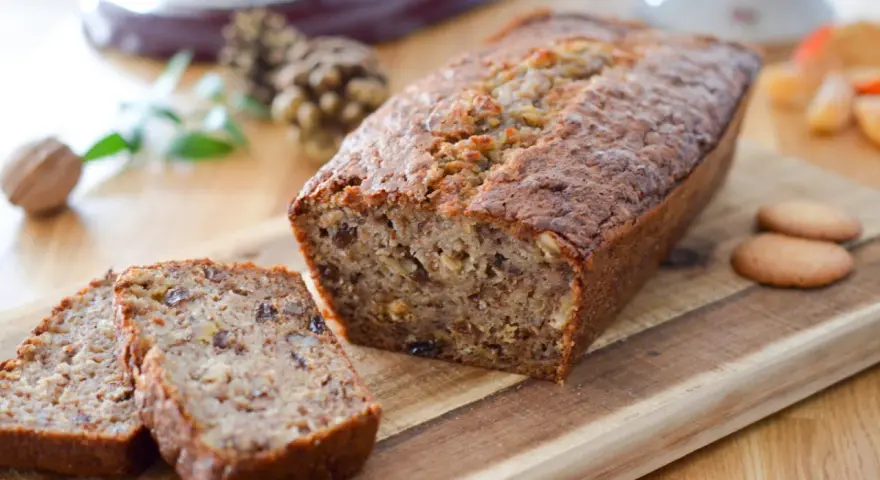 Un délicieux cake banane, coupé en tranches, sur une planche en bois. Des noix et des biscuits complètent cette gourmandise.