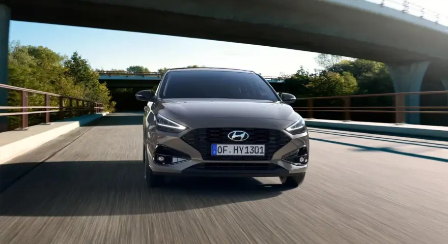 Szary Hyundai i30 1.4 benzyna pędzi po drodze pod mostem, otoczony zielenią.