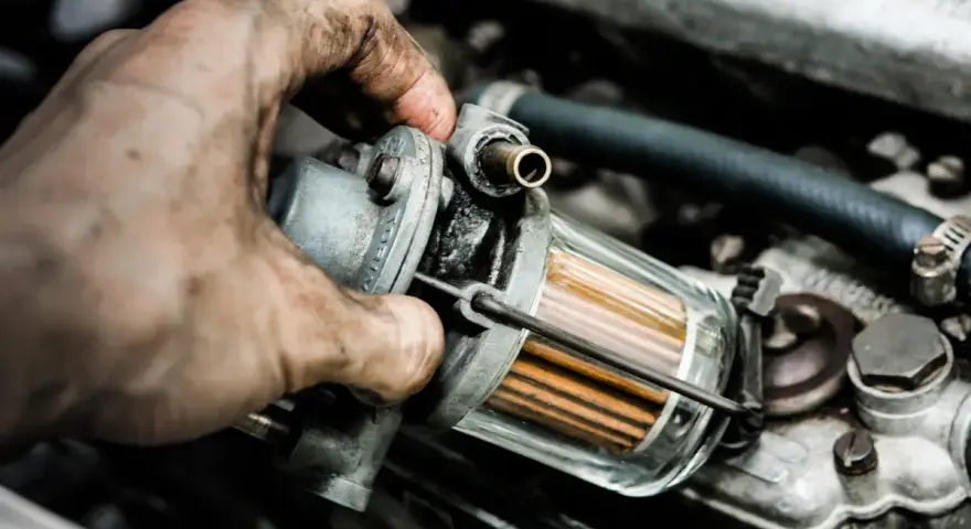 Brudna ręka mechanika wymienia filtr paliwa, by wyeliminować nierówną pracę silnika na wolnych obrotach LPG.