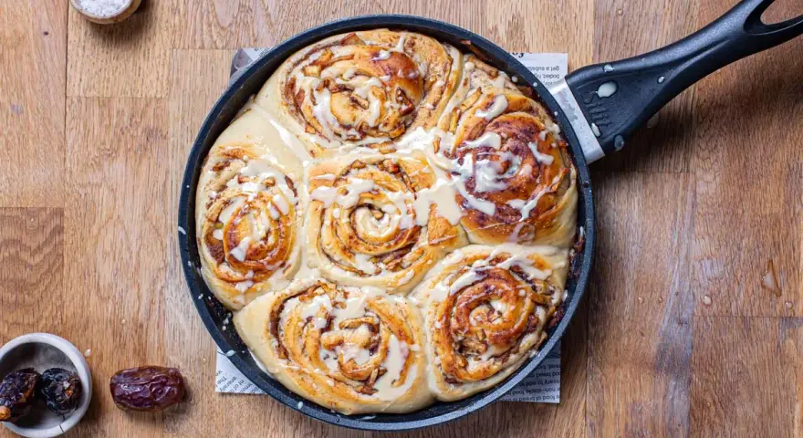 Frisch gebackene Zimtschnecken mit Apfelstückchen und Zuckerguss in einer Pfanne. Ein köstliches Apfel Zimtschnecken Rezept zum Nachbacken.