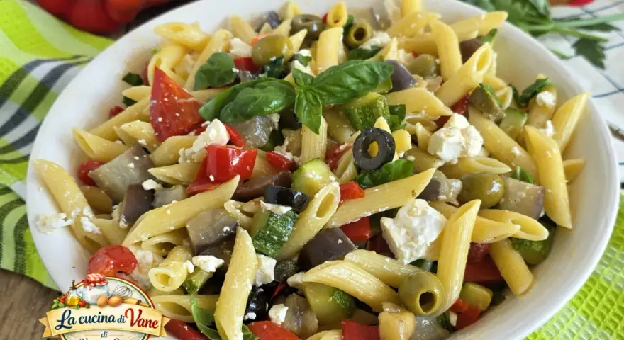 Pasta fredda con feta, peperoni, zucchine, melanzane e olive nere. Un piatto estivo colorato e saporito.