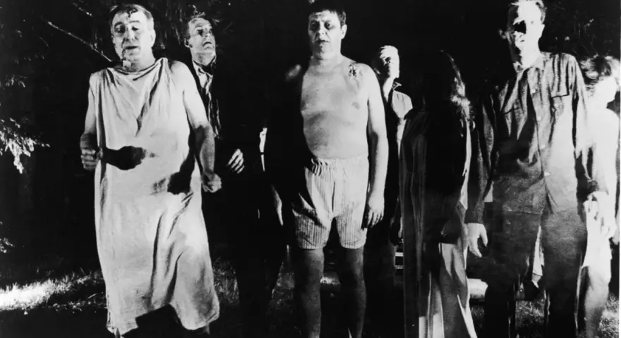 Un gruppo di persone dall'aspetto spettrale, un'immagine che evoca il significato di un b movie, cammina in un bosco di notte.