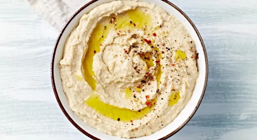 Kremowy, gładki hummus polany oliwą i posypany przyprawami. Idealny do maczania pieczywa.