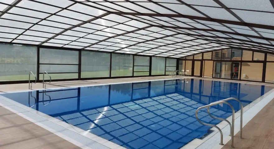 Una piscina cubierta con techo transparente y paredes de cristal, ideal para disfrutar todo el año. Estos porches para piscinas ofrecen un espacio acogedor.