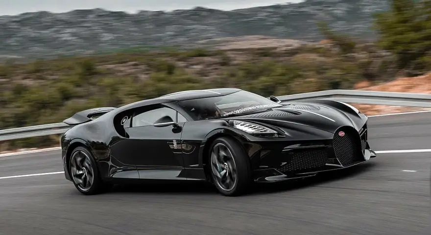 Czarny Bugatti La Voiture Noire pędzi po krętej drodze, otoczony przez górzysty krajobraz.