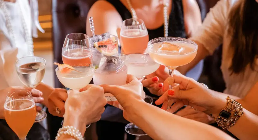 Frauen stoßen mit bunten Cocktails an. Ein fröhlicher Anlass für Day Drinking mit Freundinnen.