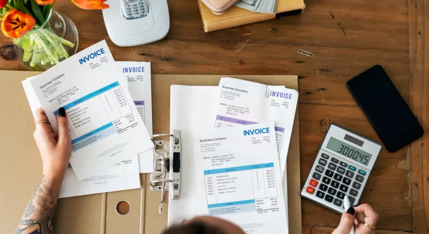 Manos revisando facturas y calculando el total. Aprende como hacer una factura a mano.