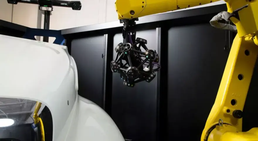 Robotyka i zaawansowany skaner optyczny badają kształt białego elementu, prawdopodobnie części samochodu.