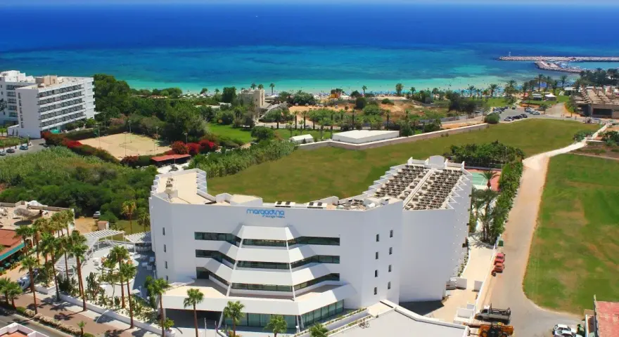 Widok z lotu ptaka na hotel Margadina Lounge Hotel z basenem i palmami, w tle błękitne morze i plaża.
