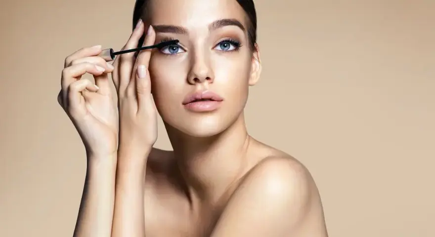 Donna con occhi azzurri applica mascara. Scopri come togliere il mascara waterproof senza irritare la pelle.