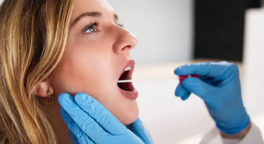 Młoda kobieta z otwartymi ustami, której gardło jest badane patyczkiem do testu strep.